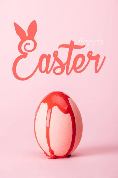 Pink chicken egg with dripping red paint on pink background with happy Easter illustration — Stock Photo