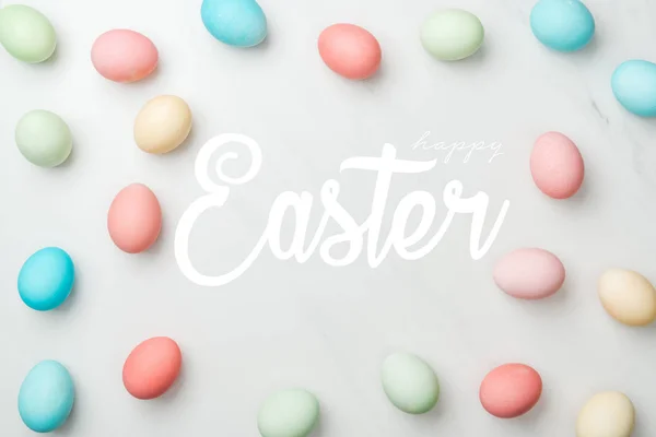 Top view of multicolored chicken painted eggs on grey background with happy Easter white lettering — Stock Photo