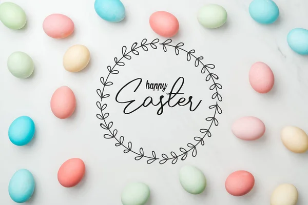 Top view of multicolored chicken painted eggs on grey background with happy Easter lettering in circle frame — Stock Photo