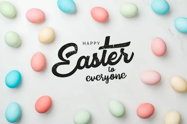 Top view of multicolored chicken painted eggs on grey background with happy Easter to everyone lettering — Stock Photo