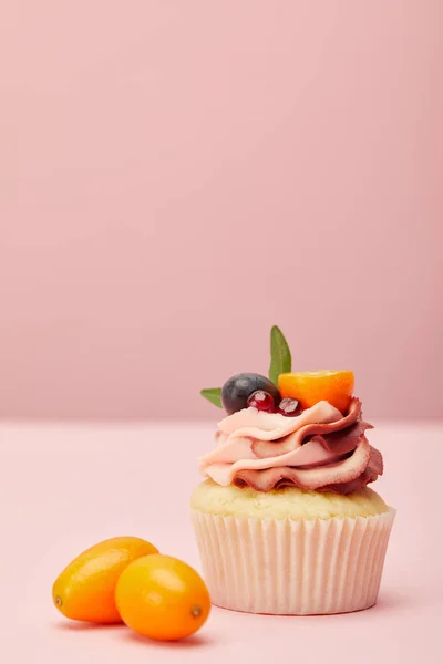 Sweet cupcake with cream and two kumquats on pink surface — Stock Photo