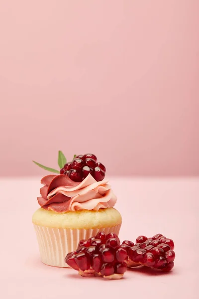 Cupcake doce com creme e granada na superfície rosa — Fotografia de Stock