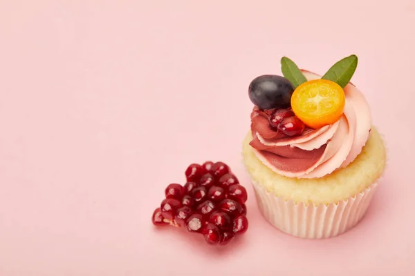 Cupcake doce com creme e granada na superfície rosa — Fotografia de Stock