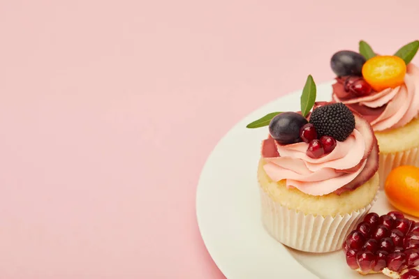 Süße Cupcakes mit Beeren und Früchten auf Teller auf rosa Oberfläche — Stockfoto