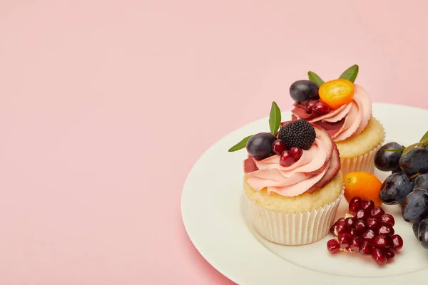Sweet cupcakes with berries and fruits on plate on pink surface — Stock Photo