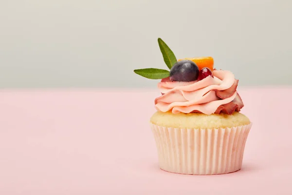 Sabroso cupcake con crema y frutas en la superficie de color rosa aislado en gris - foto de stock