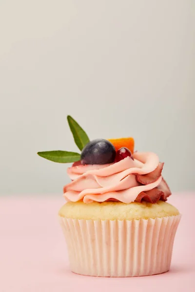 Tasty cupcake with cream and fruits on pink surface isolated on grey — Stock Photo