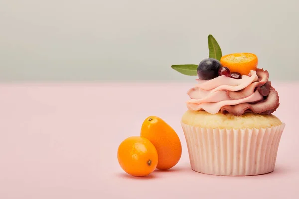 Cupcake with ripe kumquats on pink surface isolated on grey — Stock Photo