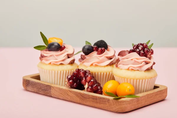 Wooden tray with sweet cupcakes on pink surface isolated on grey — Stock Photo