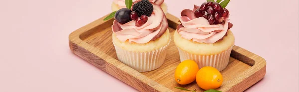 Panoramic shot of cupcakes with fruits and berries on wooden tray isolated on pink — Stock Photo