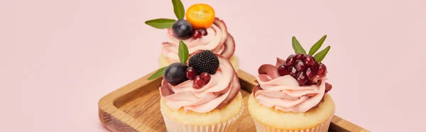 Plano panorámico de cupcakes con frutas y bayas en bandeja de madera aislada en rosa - foto de stock