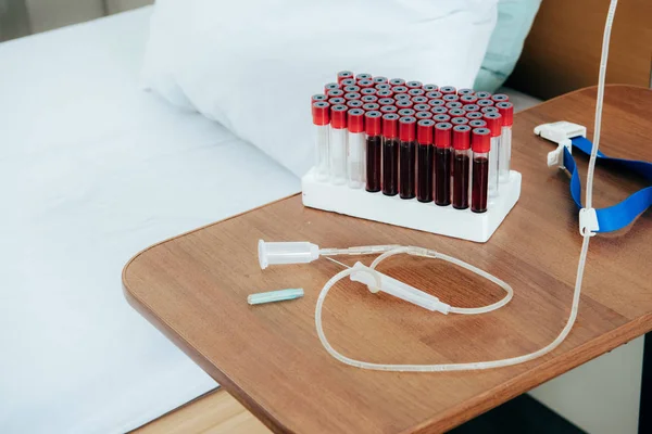 Cama con almohada, tubos de análisis de sangre, torniquete y jeringa en la sala de hospitalización - foto de stock