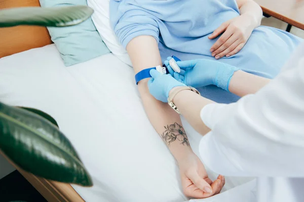 Partial view of doctor using tourniquet for blood test in hospital — Stock Photo
