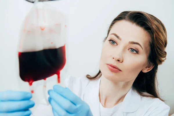 Доктор в латексных перчатках держит пакет с кровью на белом — стоковое фото