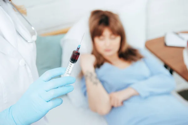 Cropped view of doctor holding syringe with blood sample and donor lying on bed — Stock Photo