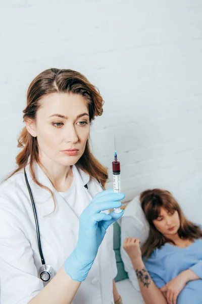 Doador deitado na cama e médico segurando seringa com amostra de sangue — Fotografia de Stock