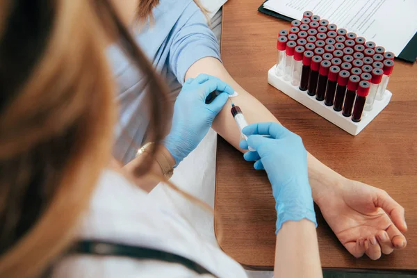 Vista recortada de donante y médico con jeringa obtención de muestra de sangre - foto de stock