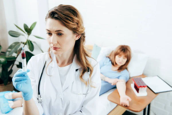 Donatore sdraiato sul letto e medico che tiene la siringa con campione di sangue — Foto stock