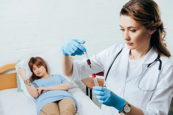 Donante en la cama y médico sosteniendo la jeringa con muestra de sangre y probeta - foto de stock