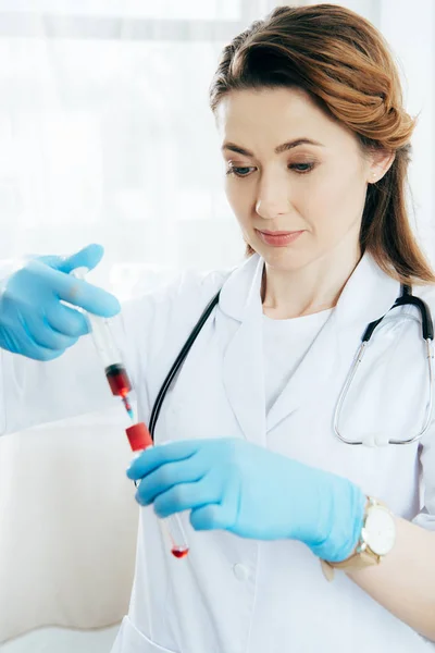 Médico en guantes de látex que sostiene la jeringa con muestra de sangre y tubo de ensayo - foto de stock