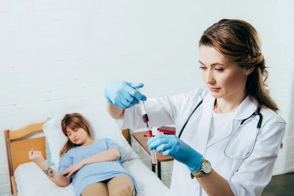 Donneur sur lit et médecin tenant une seringue avec échantillon de sang et éprouvette — Photo de stock