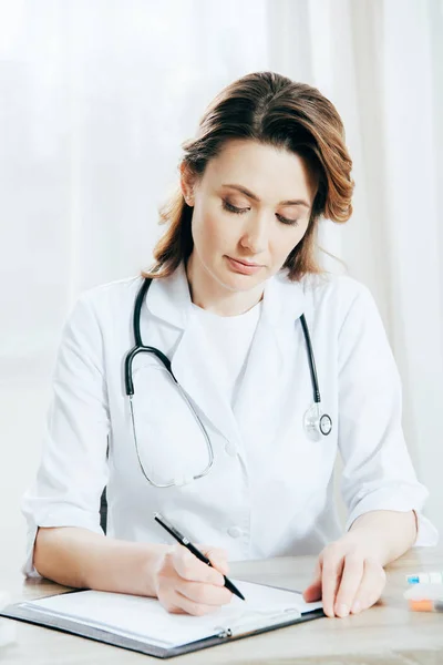 Médecin en manteau blanc écriture sur presse-papiers à la clinique — Photo de stock