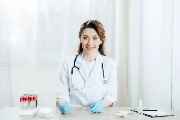 Smiling doctor holding pipette and microscope slide with blood sample — Stock Photo