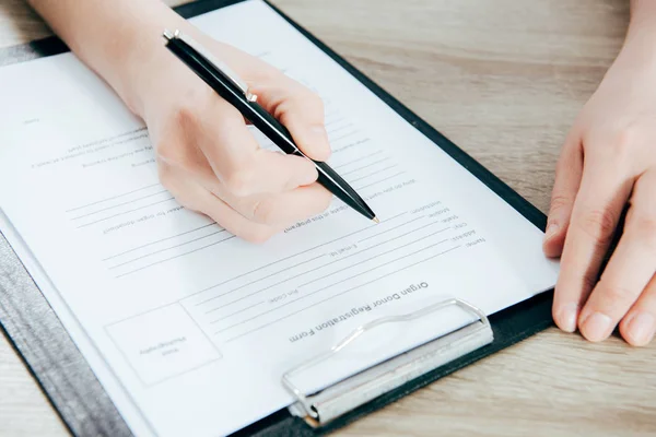 Cropped view of donor signing registration form on wooden surface — Stock Photo