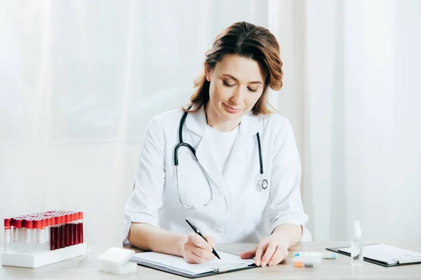 Médecin en manteau blanc écriture sur presse-papiers à la clinique — Photo de stock