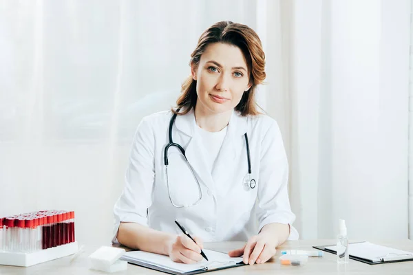 Doctor en bata blanca escrito en portapapeles en la clínica - foto de stock