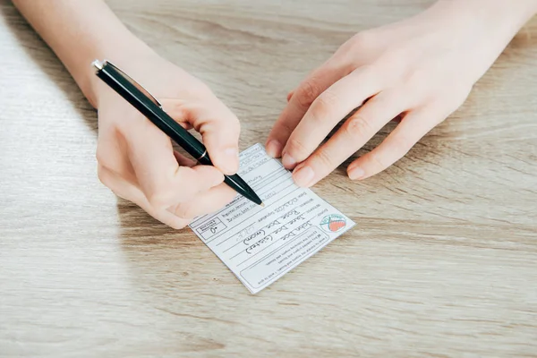 Cropped view of donor signing registration form on wooden surface — Stock Photo
