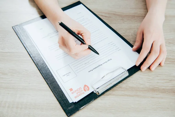 Cropped view of donor signing registration form on wooden surface — Stock Photo