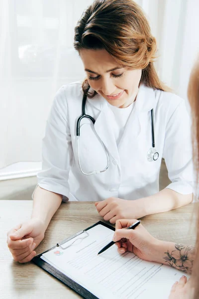 Vue recadrée du formulaire d'enregistrement de la signature du donneur et du médecin en manteau blanc — Photo de stock