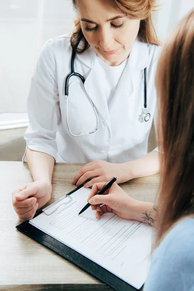Cropped view of donor signing registration form and doctor in white coat — Stock Photo