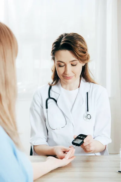 Vue recadrée du donneur et du médecin mesurant le taux de glucose avec le glucomètre — Photo de stock