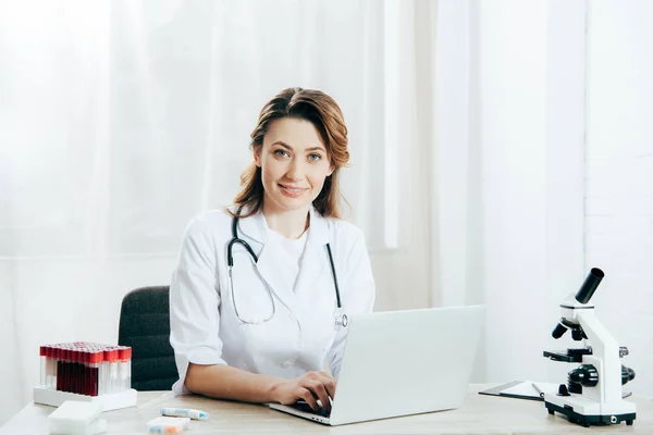 Doctor in white coat with stethoscope using laptop in clinic — Stock Photo