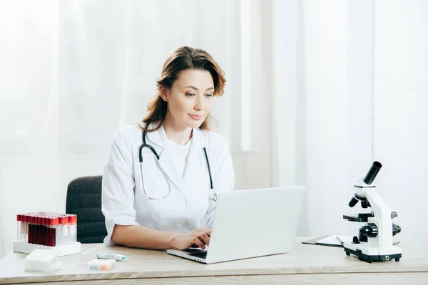 Médico em casaco branco com estetoscópio usando laptop na clínica — Fotografia de Stock