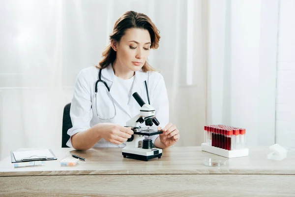 Médecin en blouse blanche en utilisant un microscope en clinique — Photo de stock