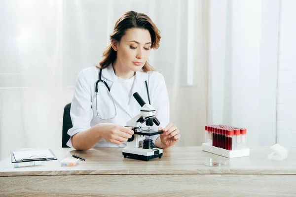 Doctor en bata blanca usando microscopio en la clínica - foto de stock