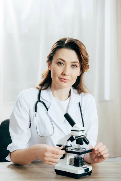 Doctor en bata blanca con estetoscopio usando microscopio en clínica - foto de stock
