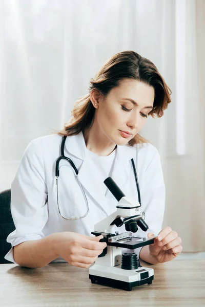 Doctor en bata blanca usando microscopio en la clínica - foto de stock