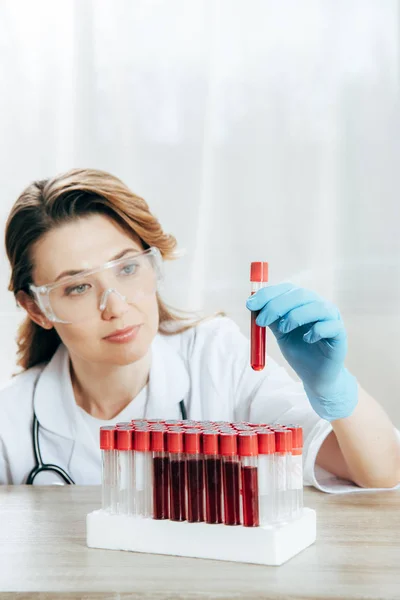 Médecin concentré dans des lunettes de protection tenant un tube à essai avec du sang — Photo de stock