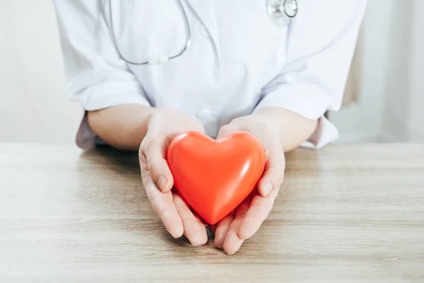 Cropped view of doctor in white coat holding plastic heart — Stock Photo