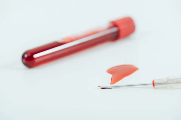 Tubo de ensayo con sangre y jeringa en superficie blanca - foto de stock