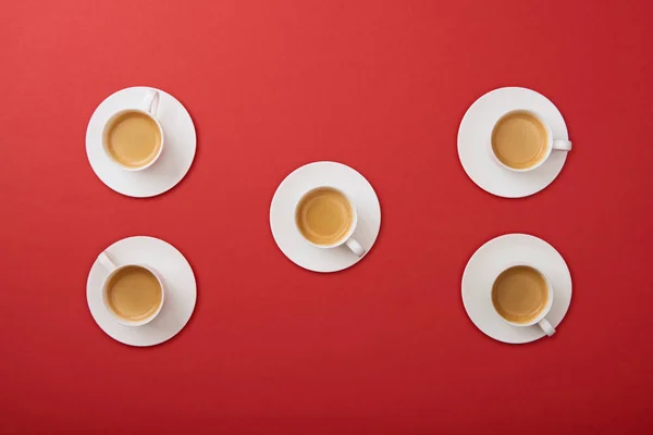 Vue de dessus des tasses blanches avec café sur soucoupes sur fond rouge — Photo de stock