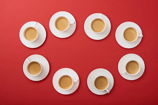Vue de dessus des tasses blanches avec café savoureux sur des soucoupes sur fond rouge — Photo de stock