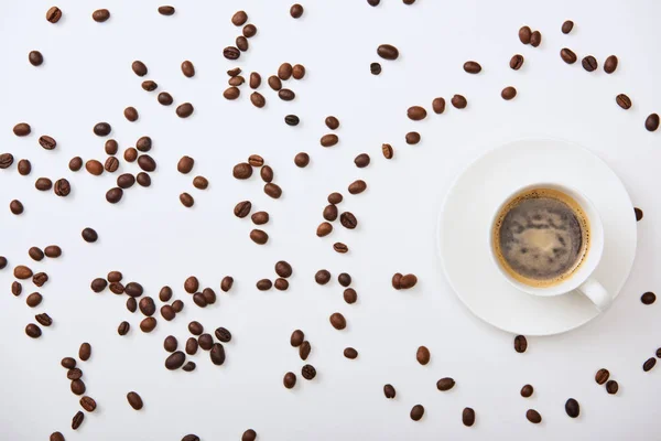 Top view of delicious coffee in cup near scattered roasted beans on white background — Stock Photo