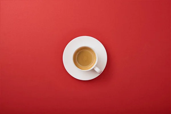 Vista superior da xícara branca com café no pires no fundo vermelho — Fotografia de Stock