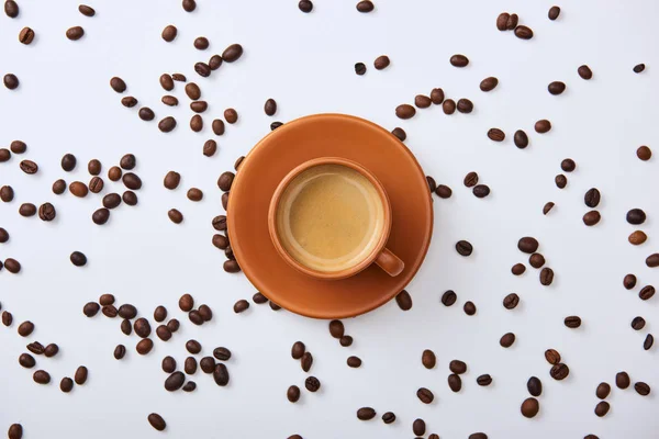 Vista superior de delicioso café na xícara perto de grãos espalhados no fundo branco — Fotografia de Stock