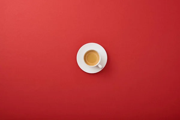 Vue du dessus de tasse blanche avec café frais sur soucoupe sur fond rouge — Photo de stock